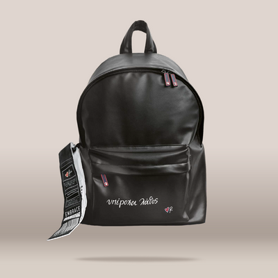 A black faux-leather backpack with a front zip pocket and top handle, featuring the brand name  in white script and a small pink heart logo. A black and white product tag is attached to the left side.
