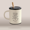 An off-white ceramic mug with a black lid and handle, featuring a light wood spoon handle and black Greek text printed on the front, set against a solid beige background.
