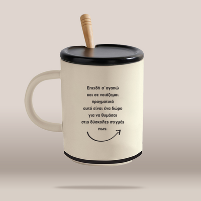 An off-white ceramic mug with a black lid and handle, featuring a light wood spoon handle and black Greek text printed on the front, set against a solid beige background.