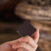 Hand holding a small black square in front of a blurred background