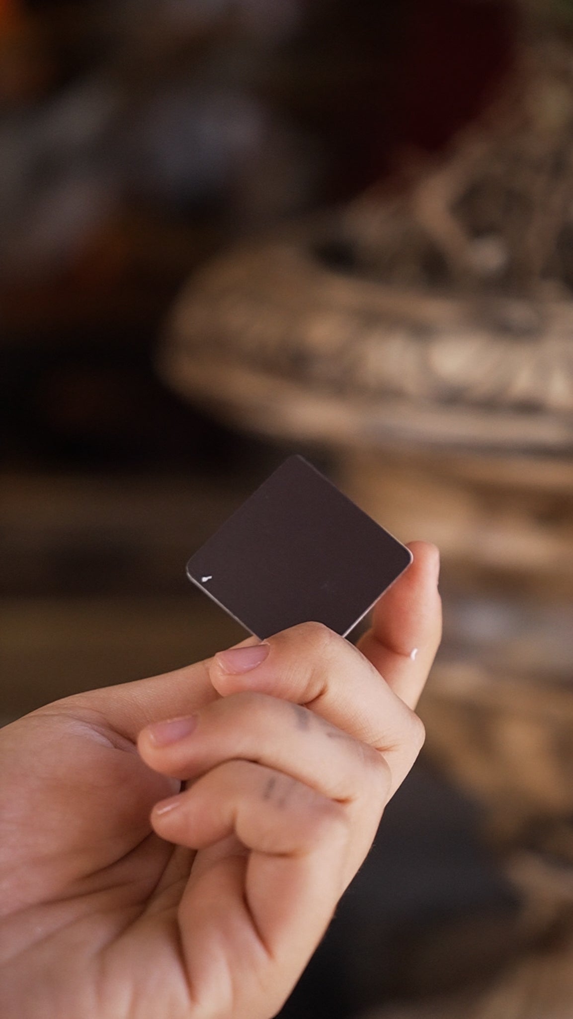 Hand holding a small black square in front of a blurred background