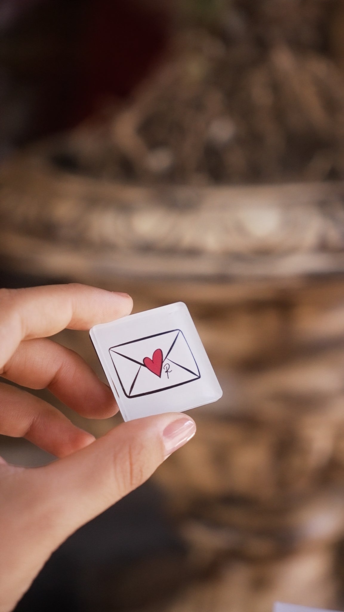 Hand holding a small card with a heart and envelope symbol against a blurred background