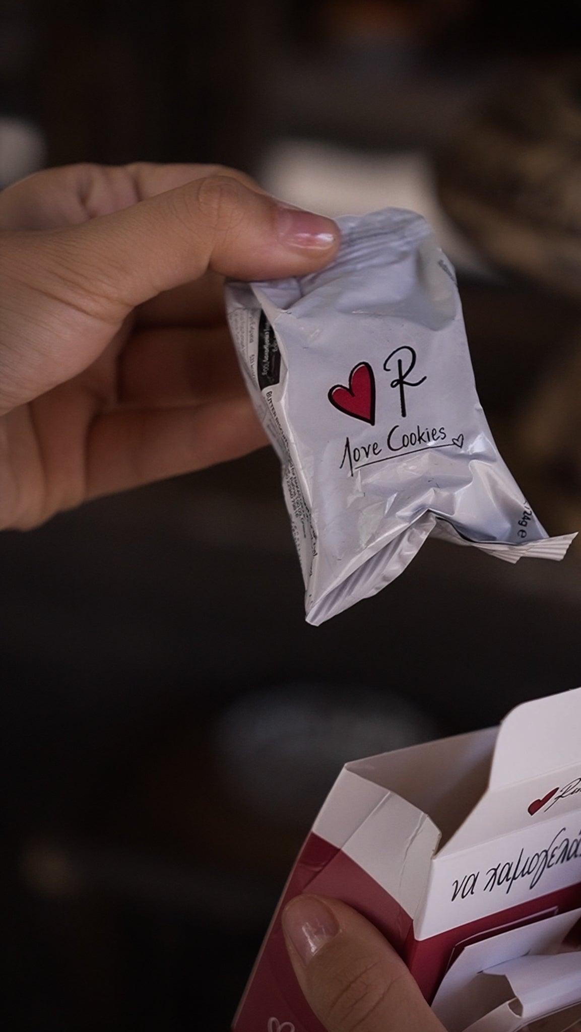 Hand holding a small white packet with a red heart and letter 'P' logo, against a blurred background.