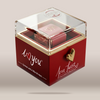 A red square chocolate gift box with a clear acrylic lid, gold trim, and a gold heart-shaped clasp. The front of the box reads 'i <heart> you' and 'Love Twist Chocolate & Necklace,' with a small necklace visible inside.