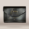 A black leather envelope-style clutch bag with gold foil script lettering on the front flap, photographed against a plain light beige background.