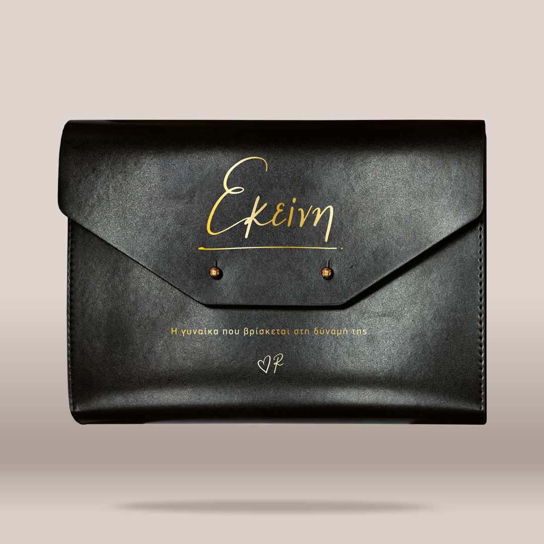 A black leather envelope-style clutch bag with gold foil script lettering on the front flap, photographed against a plain light beige background.