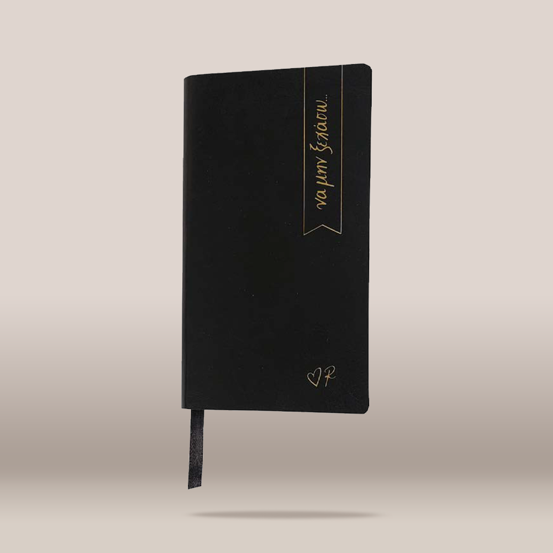 A black hardcover journal with elegant gold foil lettering on the front cover, featuring a vertical banner design with the words 'va per tecno' and a small heart monogram near the bottom. A black ribbon bookmark hangs from the bottom edge, set against a clean, neutral beige background.