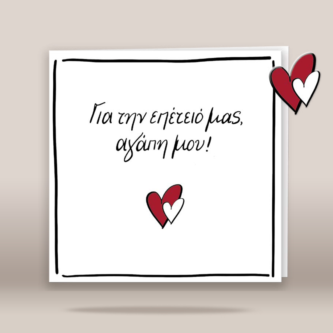 A square white greeting card with a hand-drawn black border and Greek text reading 'Για την επέτειο μας, αγάπη μου!' with small red-and-white heart illustrations, shown on a warm beige background.
