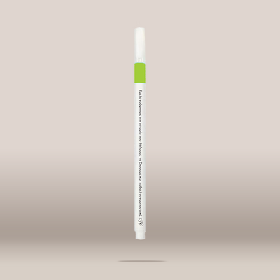 A single white cosmetic pen-style applicator with a bright green band near the top and black printed text, shown centered against a soft beige gradient background.