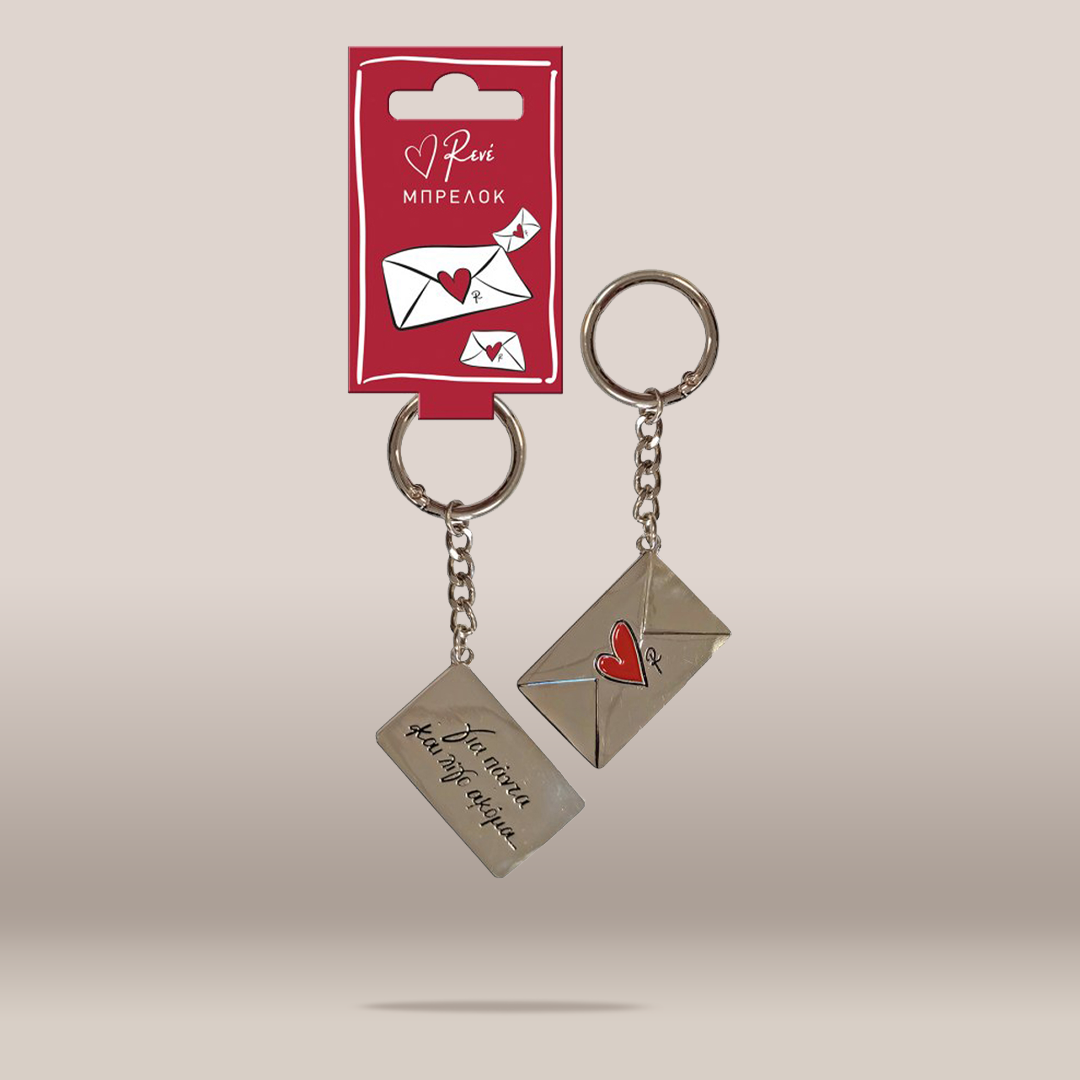 Two silver-toned metal keychains with envelope-shaped charms and a small red heart detail, shown hanging from a red branded card on a plain light beige background. One charm is engraved with text, and the other has a red heart on its envelope.