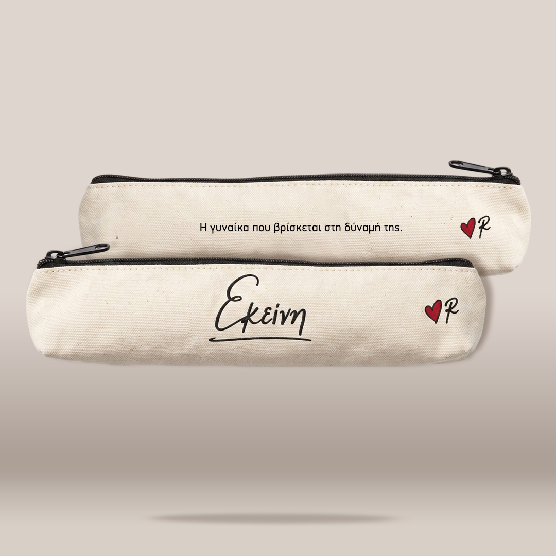 Two cream-colored canvas pencil cases with black zippers, displayed against a neutral beige background. The top case features Greek text in black, while the bottom case has the Greek word 'Ekeimena' (meaning 'future') in black script, a small red heart with a black 'P' inside, and a subtle shadow underneath.