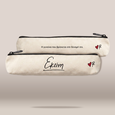 Two cream-colored canvas pencil cases with black zippers, displayed against a neutral beige background. The top case features Greek text in black, while the bottom case has the Greek word 'Ekeimena' (meaning 'future') in black script, a small red heart with a black 'P' inside, and a subtle shadow underneath.