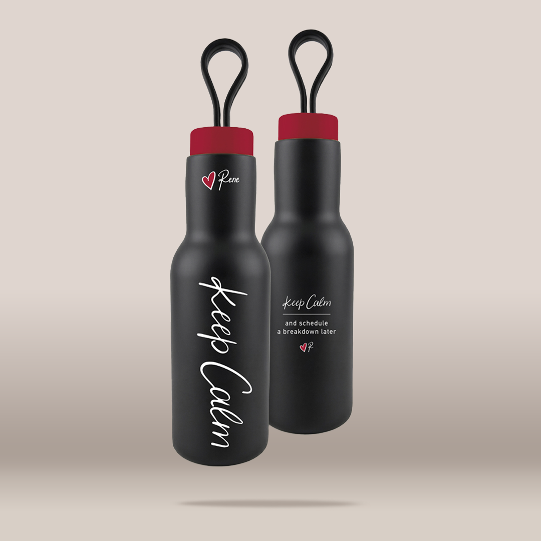 Two matte black insulated water bottles with red caps and black loop handles, shown on a warm beige studio background. One bottle has white script text reading 'Keep Calm' and a small red heart logo with 'Pure' above it.