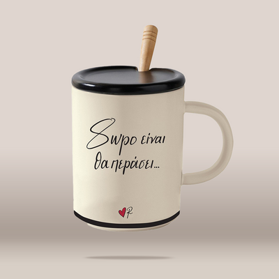 An off-white ceramic mug with a black lid and handle, featuring a light wood spoon handle and black Greek text printed on the front, set against a solid beige background.
