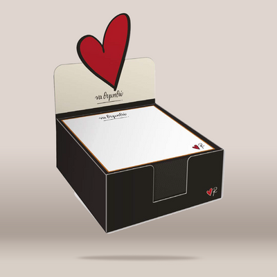 A boxed stationery set shown on a plain beige background. The product includes a black display box with a cream-colored inner tray and a large red heart graphic on the back panel, plus matching white paper sheets with small red heart details.