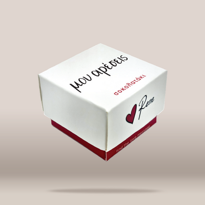 A white square gift box with red accents and Greek text, including the name 'Rene' next to a small red heart, shown floating against a light beige background.