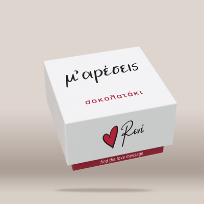 A white square gift box with Greek text 'ΜΟΥ ΑΡΕΣΕΙΣ' in black and red, featuring the Revé logo with a red heart and the phrase 'find the love message' on a light beige background.