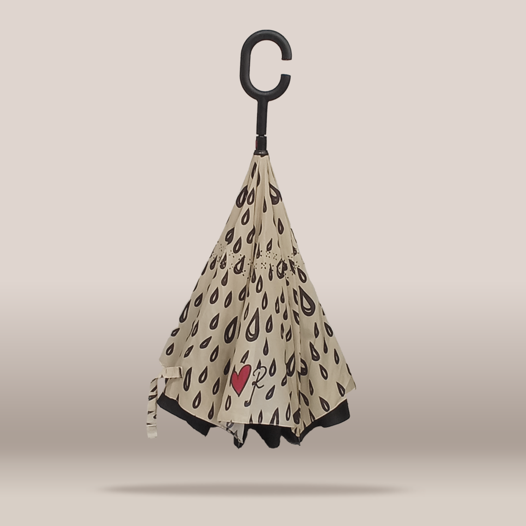 A reverse umbrella with a beige background and a black raindrop pattern, featuring a small red heart with a white key in the center. The handle is a black C-shaped hook, shown against a neutral beige background.