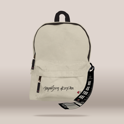 An off-white canvas backpack with black trim, featuring a front zippered pocket with the text  in black script, and a black hanging strap with the text 'BE AS YOU ARE'.