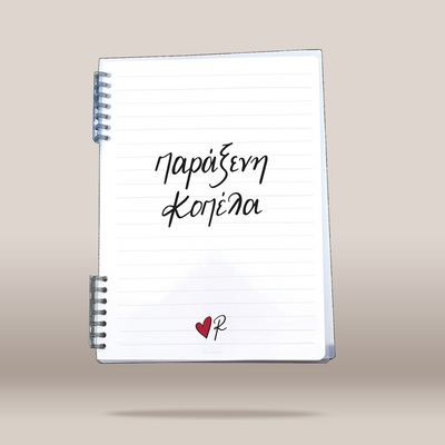 A white spiral-bound lined notebook floating against a warm beige gradient background. The notebook has black handwritten-style Greek text on the cover and a small red heart with a black script mark near the bottom.