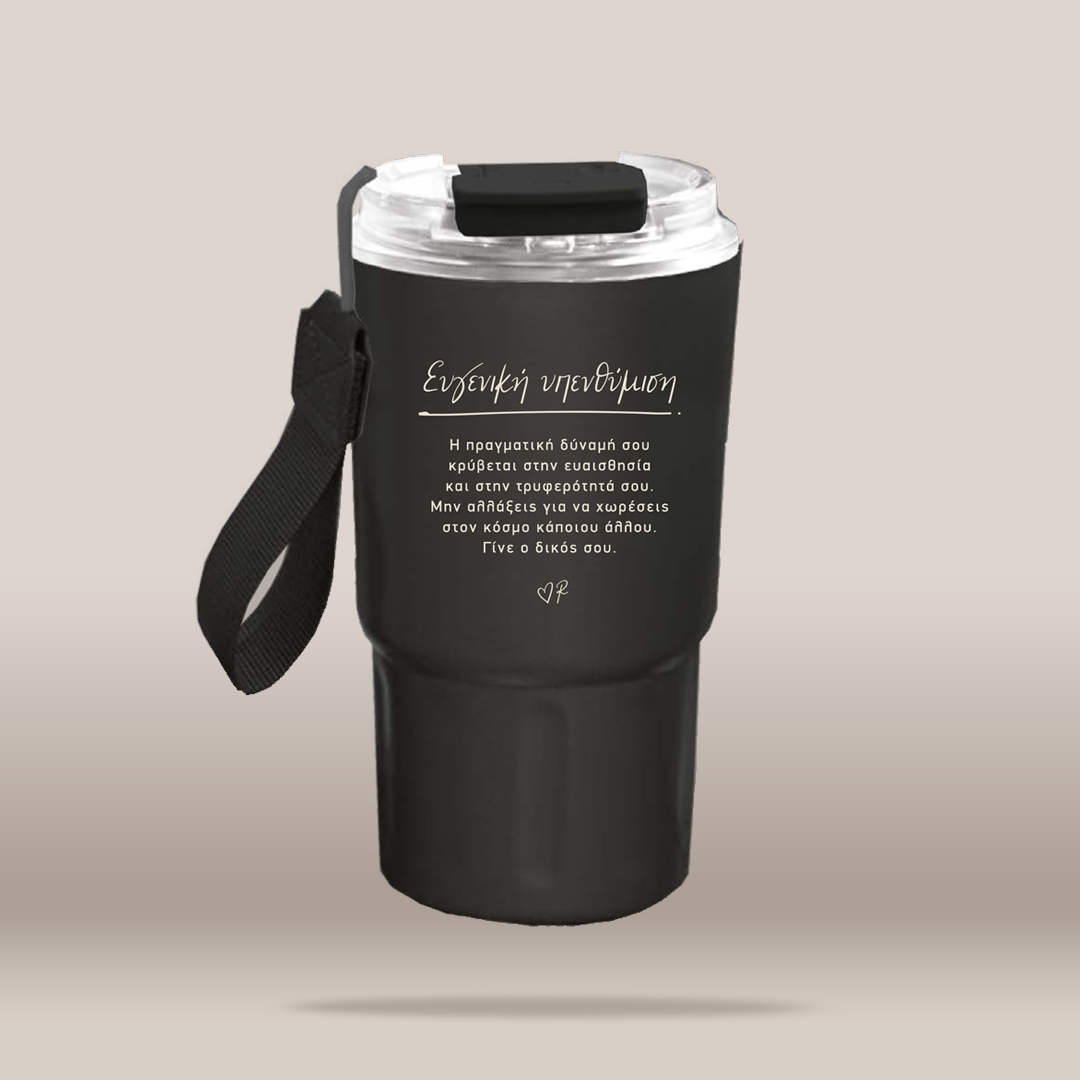 A matte black insulated travel tumbler with a clear lid, black carrying strap, and white Greek text printed on the front, shown on a plain beige background.