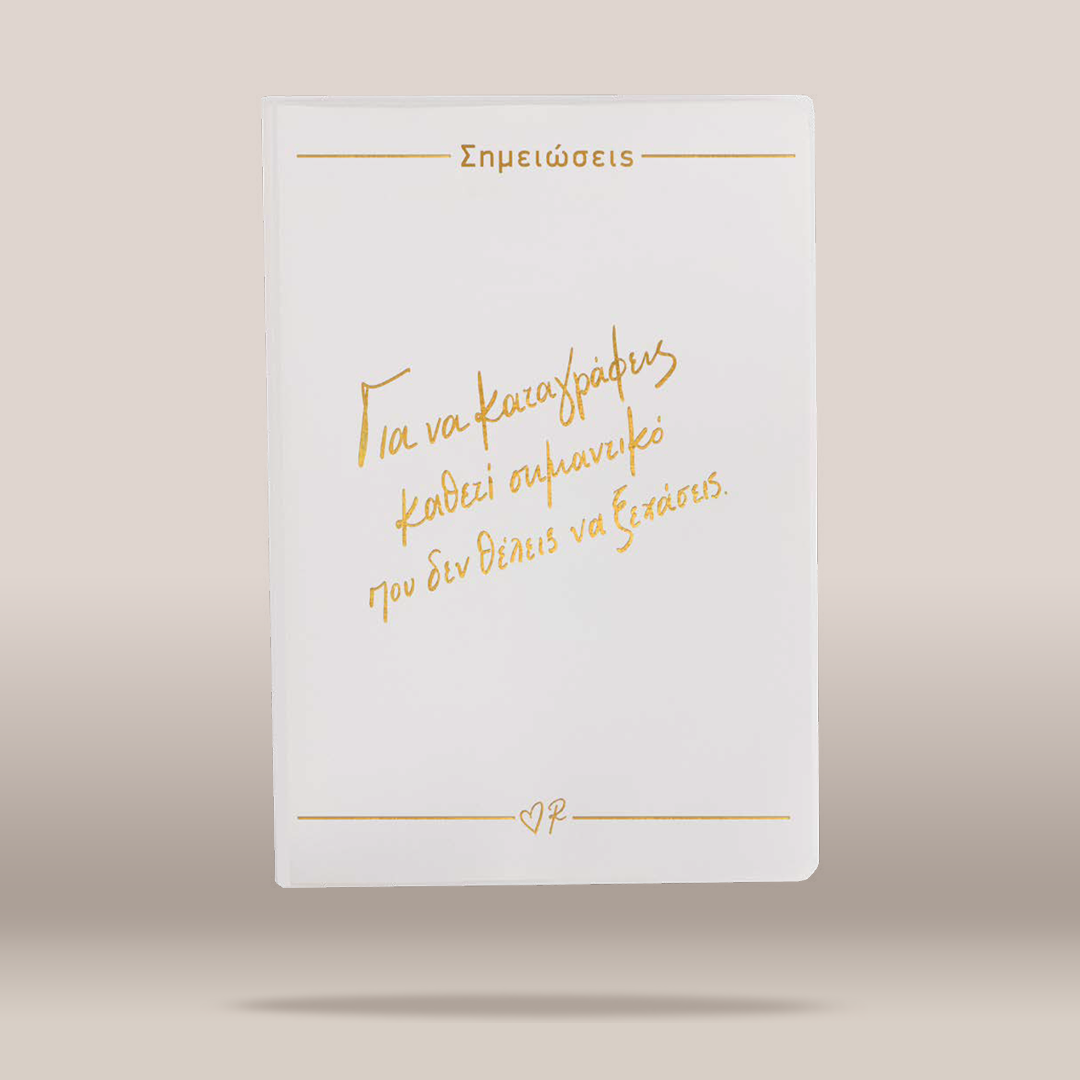A white rectangular card or notebook cover with gold foil Greek text and thin gold lines, centered on a warm beige background.
