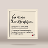 A square cream-colored card or print with black Greek text and a thin rectangular border, shown centered on a light warm gray background with a soft shadow underneath.