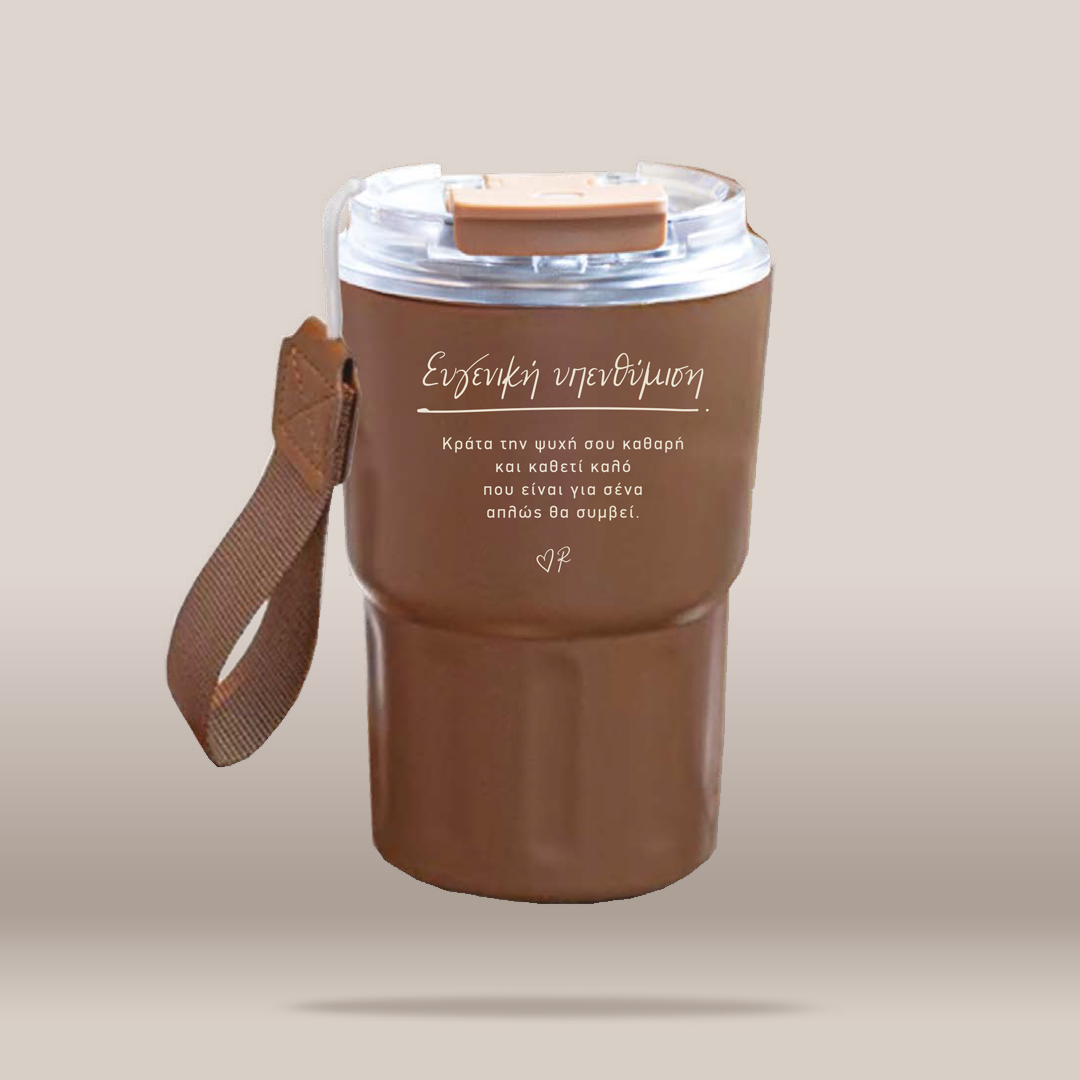 A brown insulated travel tumbler with a clear lid, brown carrying strap, and white Greek text printed on the front, shown on a plain beige background.