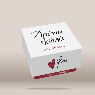 A white square gift box with black and red text, featuring the Revé logo and a red heart on the front, shown floating against a warm beige gradient background.