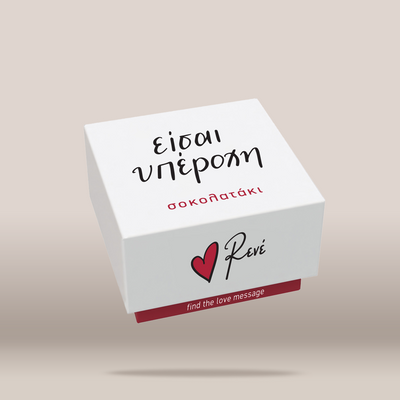 A white square gift box with black and red printed text and a red heart logo, shown floating on a plain warm beige background. The visible branding reads Revé.