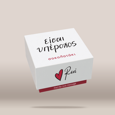 A white square gift box with black and red printed text and a red heart logo, shown floating on a warm beige background. The top reads 'EISAI YPEROXOS' and the front shows the Revé brand name with a red heart logo and the phrase 'find the love message'.