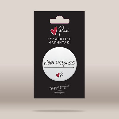 A white circular pin-back button with black script text and a small red heart logo, mounted on a black retail card. The card shows the brand name 'Renei' and Greek text, photographed against a plain light beige background.
